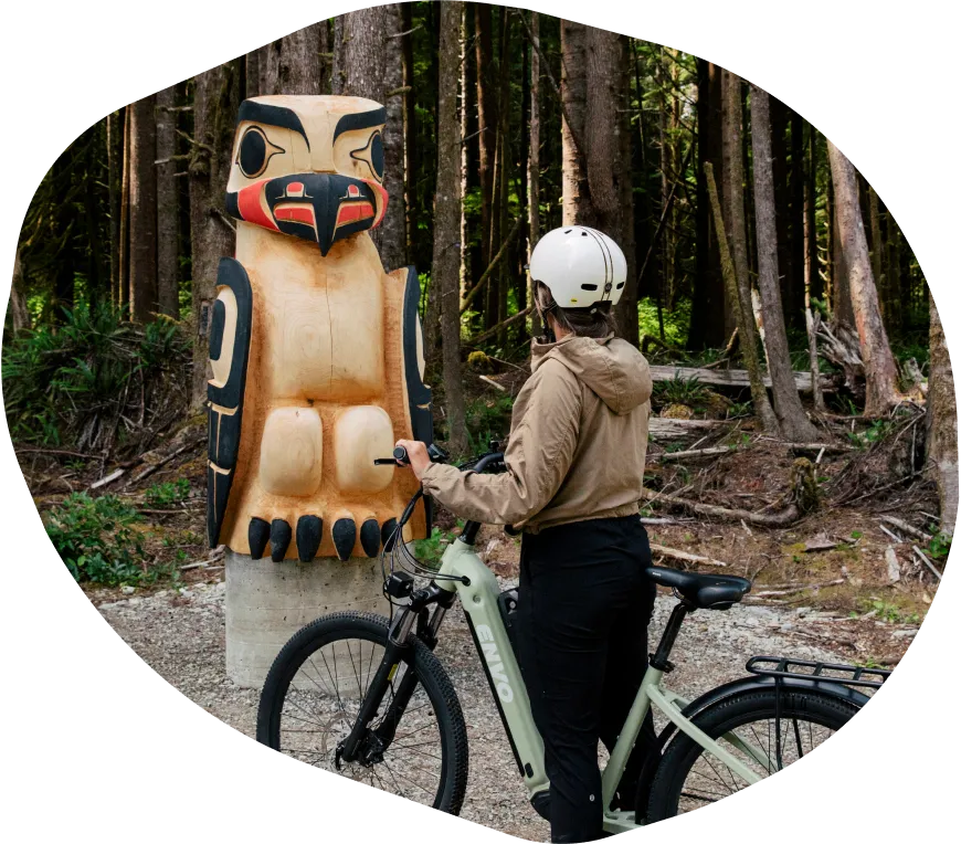 A woman cyclist standing next to a large carved totem pole